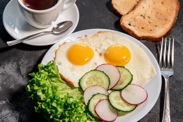 Two fried eggs, lettuce, cucumber and radish slices on a white plate, toast and a cup of tea or coffee. Scrambled eggs. Breakfast. Healthy eating. Close-up