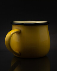 Close up shot of a yellow ceramic mug isolated on a dark background © Cristian Muñoz Gallardo/Wirestock