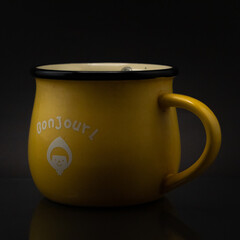 Side shot of a bonjour yellow mug isolated on a dark background © Cristian Muñoz Gallardo/Wirestock