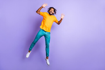 Fototapeta na wymiar Full size photo of nice optimistic brunette hairdo guy jump wear orange t-shirt pants isolated on lilac color background