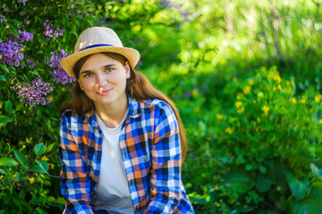 Defocus young summer woman. Beautiful woman in checkered shirt and hat with lilac bunch and meadow of flowers in spring garden, portrait of young women. Out of focus