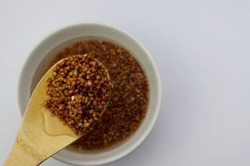 Washed buckwheat groats in a wooden spoon on a white background. Buckwheat in water.