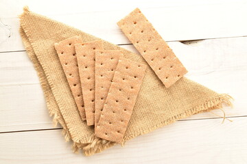 Several light brown multi-grain rye crispbreads on a jute napkin, close-up, on a wooden table, top view.