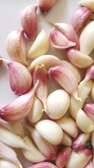 Top view close up of red-white garlic cloves on white ceramic background.