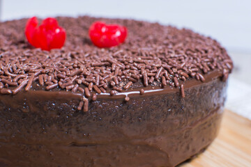 Big Chocolate cake, decorated with chocolate chips and cherry on wooden background