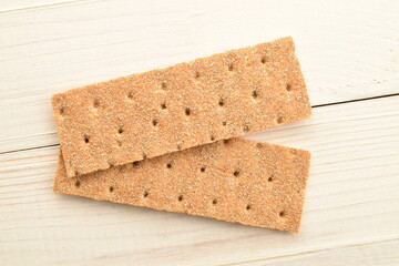 Two light brown multi-grain rye crispbreads on a wooden table.