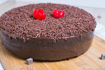 Big Chocolate cake, decorated with chocolate chips and cherry on wooden background