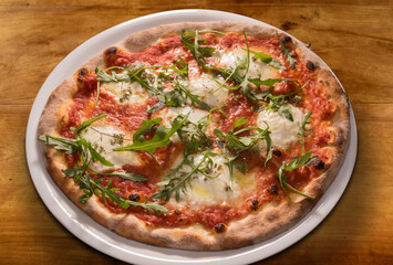 Pizza with arugula leaves, tomato sauce, mozzarella cheese in white plate on wooden table, top view
