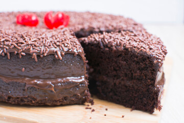Big Chocolate cake, decorated with chocolate chips and cherry on wooden background