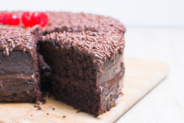 Big Chocolate cake, decorated with chocolate chips and cherry on wooden background