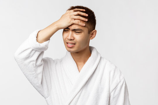 Beauty, Spa And Leisure Concept. Uset Distressed Asian Man Feel Bad, Hold Hand On Head And Shaking In Denial, Grimacing Gloomy, Standing Sad And Uneasy Over White Background In Bathrobe