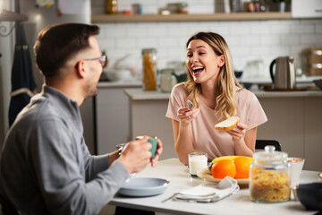 Beautiful woman enjoying in breakfast with her boyfriend. Happy young couple drinking coffee and eating sandwich at home