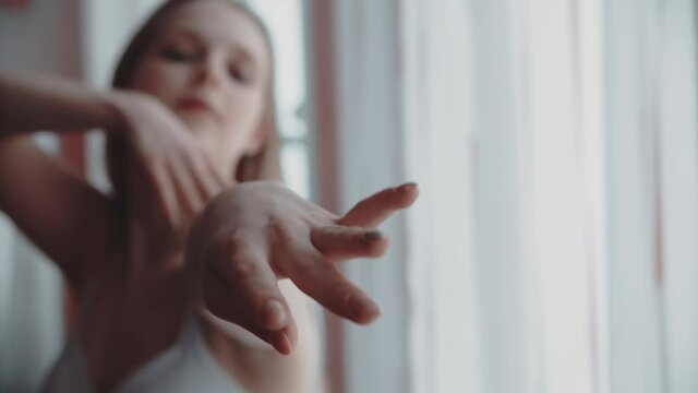 The dancer dances near the window, beautifully raises her hands and performs dance moves in the dance hall.
