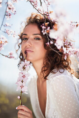 Obraz na płótnie Canvas spring portrait of a beautiful woman with curly hair next to tree flowers