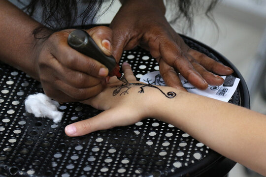 the process of creating a child's henna tattoo in the form of a lizard on the arm
