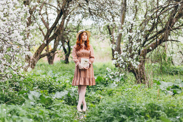 Fototapeta na wymiar Red-haired girl walks in a spring blooming apple orchard