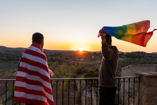 Two men holding rainbow pride and American flag at sunset.Lifestyle of LGBT and Usa concept.