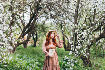 Fototapeta na wymiar Red-haired girl walks in a spring blooming apple orchard