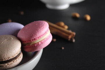 Macaroons on a gray plate at the back stands a cup of coffee or tea coffee beans and cinnamon sticks on a black background with a place for text and with a copyspace