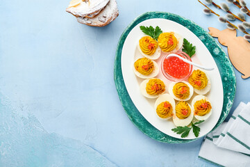 Stuffed eggs with red caviar and paprika on blue plate for appetizer easter table, top view, copy space. Traditional dish for Happy Easter holiday.