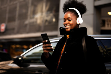 Young african woman outdoors. Beautiful woman listening to music while walking through the city