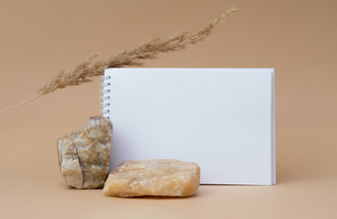 White blank sheet of notepad, stones, dry sprig of grass, on beige background. Copy space, template for your ad, mockup