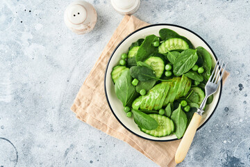 Green vegetable salad with spinach, avocado, green peas and olive oil in bowl on light gray slate, stone or concrete background. Top view with copy space. Green vegetables for diet concept.