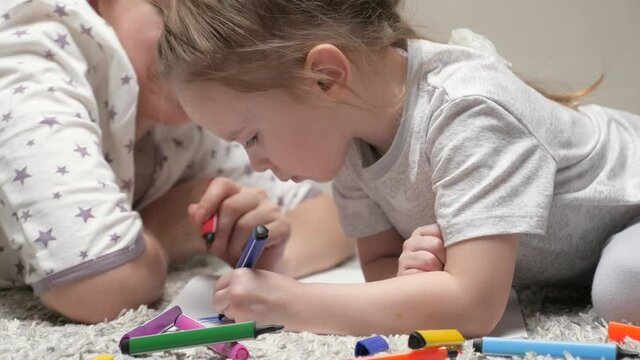 Child and Mom, nanny, teaches girl to draw. Happy family playing together at home on floor. A mother helps her daughter learn to draw on paper, coloring with multi-colored pencils and felt-tip pens.