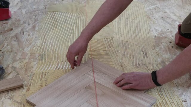 Laying parquet in an apartment during renovation. Herringbone parquet video 4k. Worker installing wood parquet.