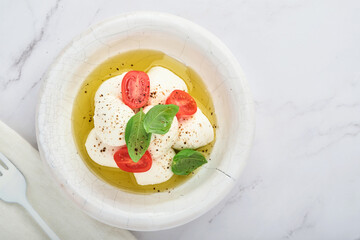 Caprese salad. Mozzarella cheese with basil  and cherry tomato in white ceramic plate and tomato cherry on slate stone background, copy space. Mock up.