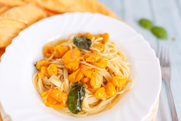Pasta, spaghetti with yellow tomato in white plate. Blue background. Top view. Close up.