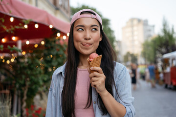 Portrait of beautiful asian woman eating ice cream on the street.  Emotional hipster wearing casual...
