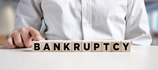 Businessman pressing his finger on the wooden cubes with the word bankruptcy.