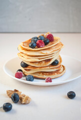 Freshly cooked delicious pancakes with honey, walnut, honey, raspberries and blueberries for breakfast.