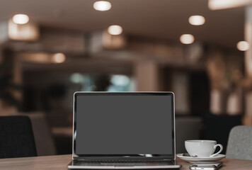 Mockup of laptop computer with empty screen with coffee cup and smartphone on table of the coffee shop background