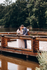 The newlyweds are resting on the wooden pier of a small lake. Hot summer day.