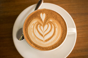 Hot coffee latte with latte art milk foam in cup mug on wood desk on top view. As breakfast In a coffee shop at the cafe,during business work concept