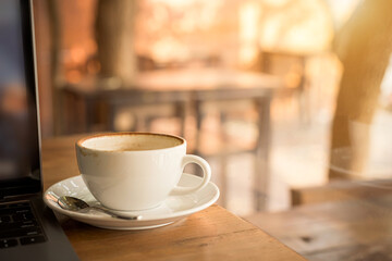 Close-up of Hot coffee latte with latte art milk foam in cup mug and laptop computer on wood desk office desk in coffee shop at the cafe,during business work concept