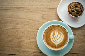 Hot coffee latte with latte art milk foam in cup mug and Homemade Banana cup cake on wood desk on top view. As breakfast In a coffee shop at the cafe,during business work concept