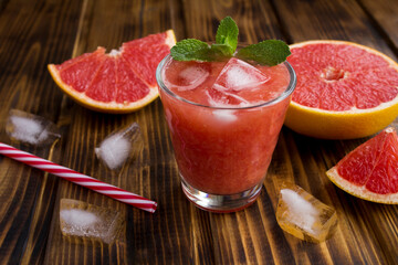 Close-up on grapefruit smoothie with ice in a drinking glass on the wooden background