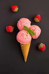 Close-up on strawberry ice cream in a waffle cone on the black background. Location vertical.