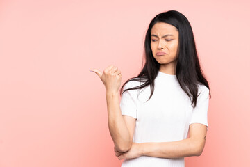Teenager Chinese woman isolated on pink background unhappy and pointing to the side
