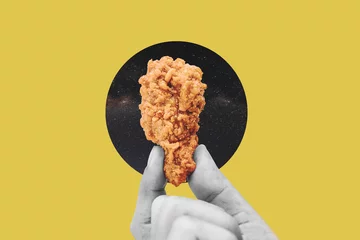 Poster Hand holding fries chicken drumstick, on yellow background © SasinParaksa