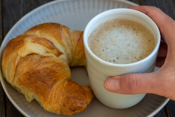 hand holding cup of milk coffee croissant