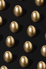 Creative gold eggs pattern over dark black background. Minimal black luxury Easter concept.
