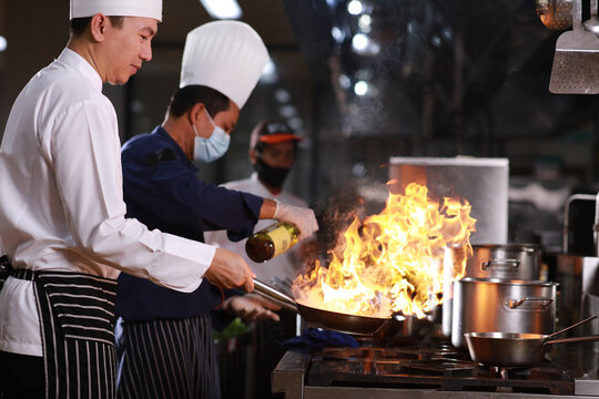 Closeup chef hands cook food with fire. Chef man burn food at professional kitchen