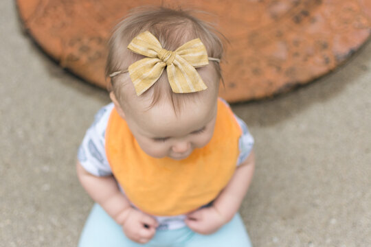 10 month old baby with yellow bow in hair sitting on front stoop of home; fine baby hair