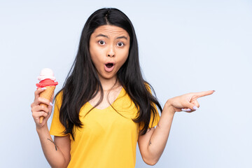 Teenager Asian girl with a cornet ice cream isolated on blue background surprised and pointing side