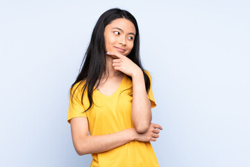 Teenager Chinese woman isolated on blue background looking to the side and smiling