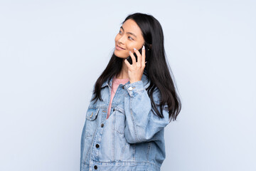 Teenager Chinese woman isolated on blue background keeping a conversation with the mobile phone with someone